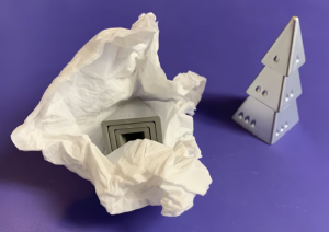 a nest of silver pyramids, viewed from the bottom, wrapped in white tissue paper, next to a tree of silver pyramids, all on a purple surface